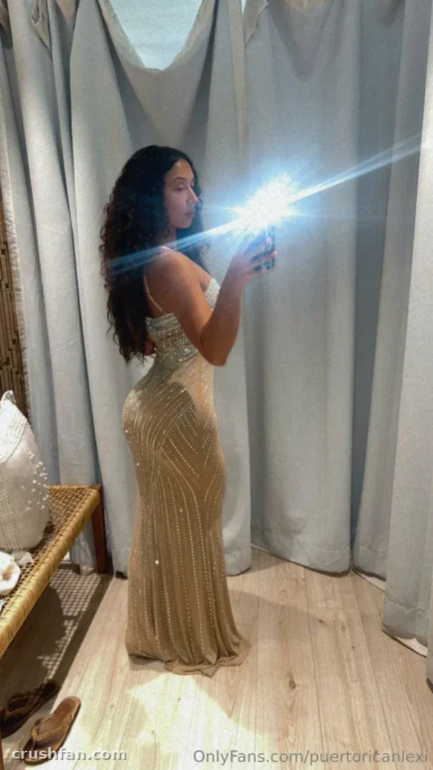 Lexi in a beaded champagne gown taking a mirror selfie beside pale curtains