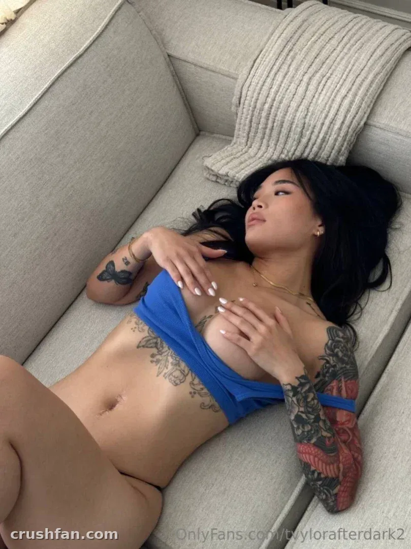 Creator nhi reclining on a grey sofa wearing a blue top with visible arm tattoos.