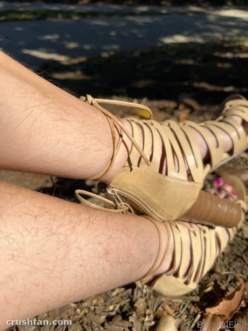 Close-up of crossed legs in beige strappy heels resting outdoors in sunlight.