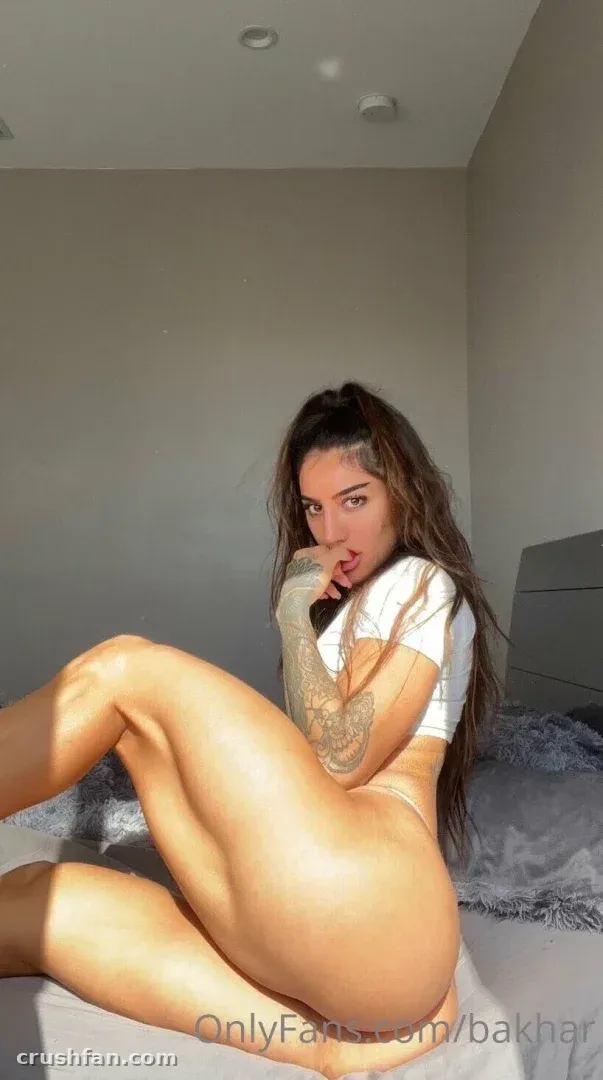 Bakharnabieva в белом кроп-топе сидит на кровати в мягко освещённой комнате