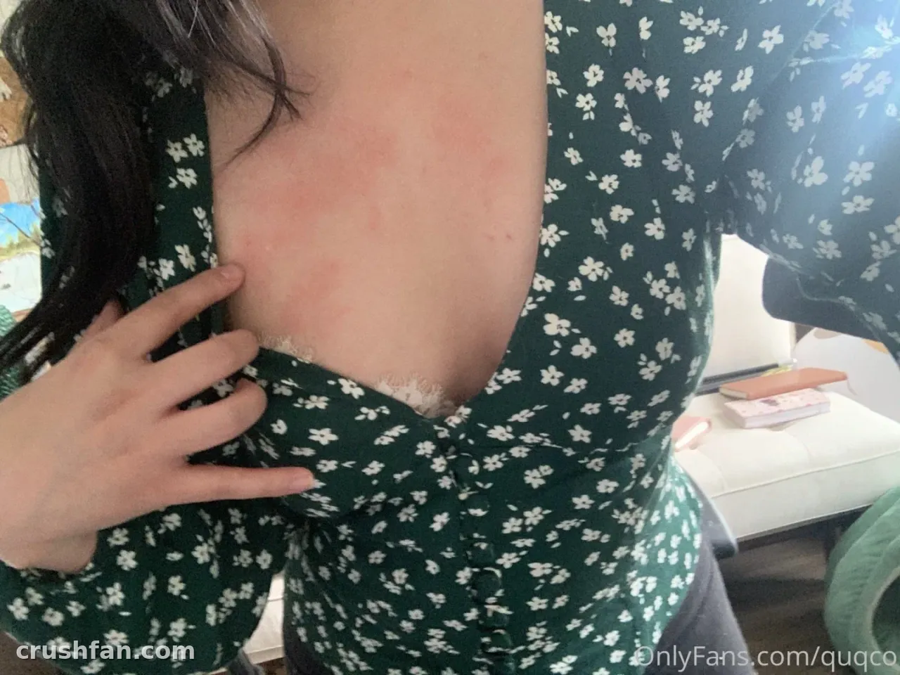quqco in a dark green floral top, hand near the neckline, indoors