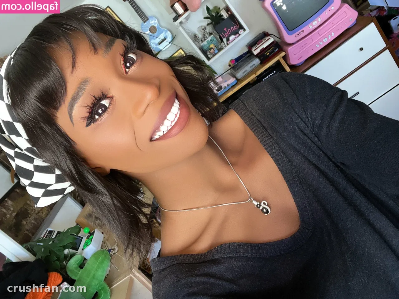 Selfie de close de uma mulher sorridente com uma faixa xadrez em um quarto colorido.