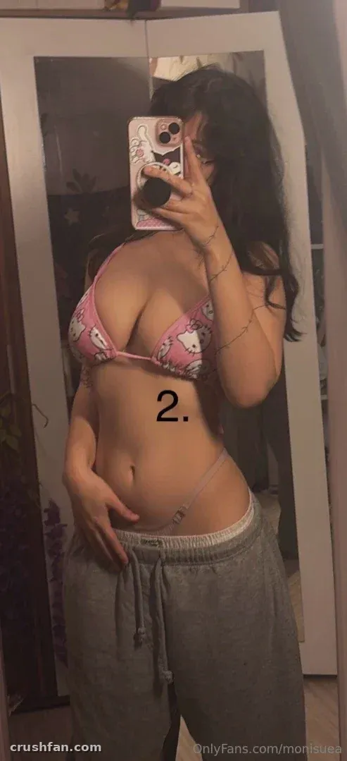 Woman in a pink bikini top and grey sweatpants taking a mirror selfie with a patterned phone case.