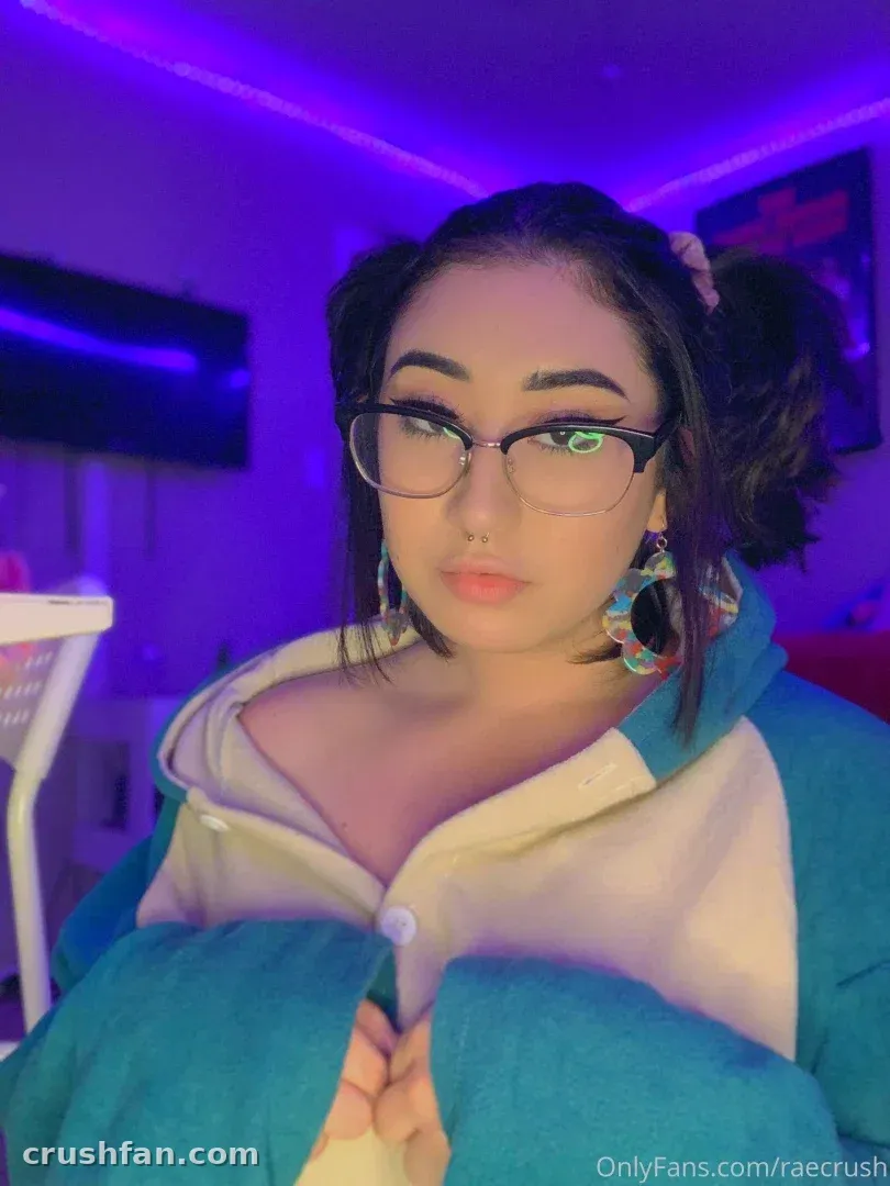 Rae in glasses and a teal jacket under purple indoor lighting