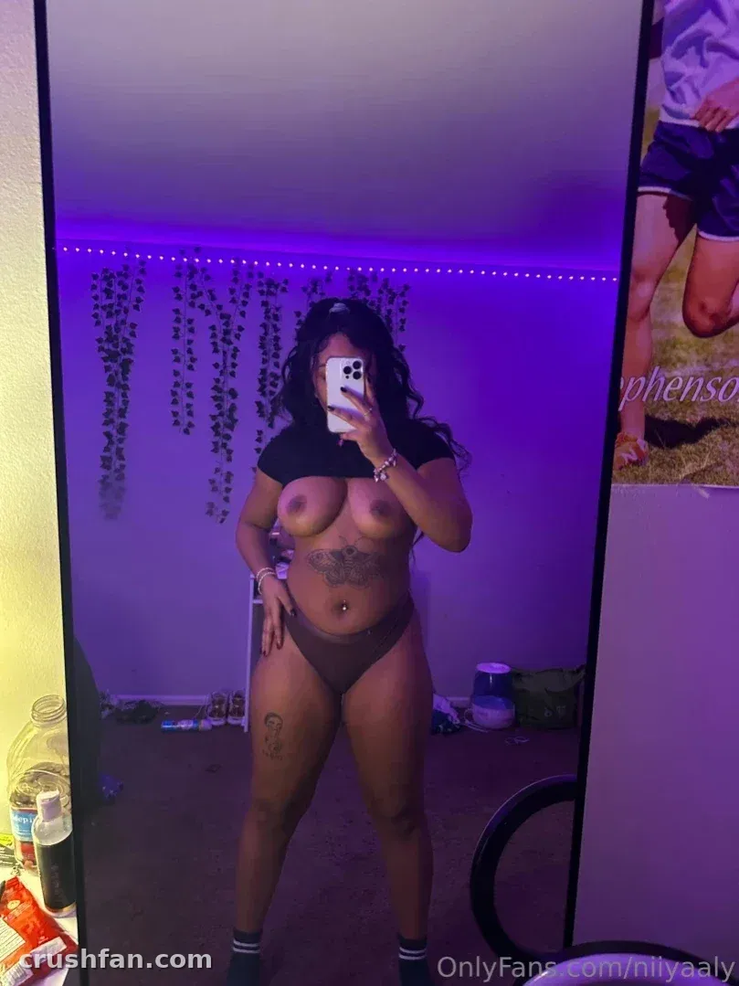 Creatorin in einem violett beleuchteten Raum beim Mirror-Selfie in schwarzem Top und Bikinihöschen