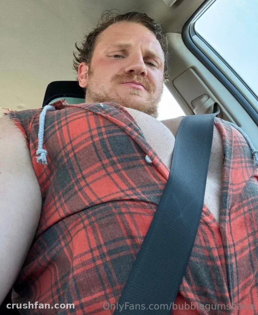 bubblegumshane em uma camisa xadrez vermelha sentado em um carro com um cinto de segurança cruzando o peito.