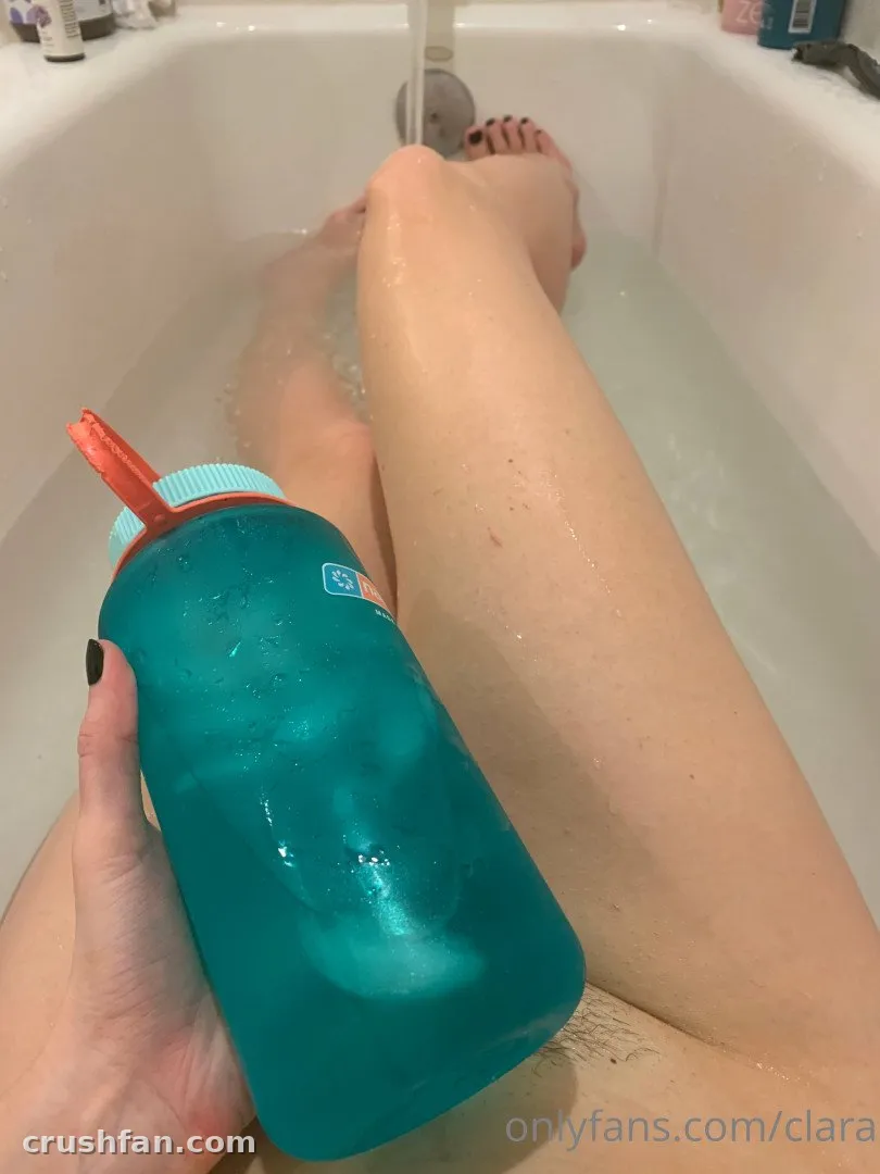 Clara dans une baignoire tenant une bouteille d'eau bleu sarcelle avec un bouchon orange