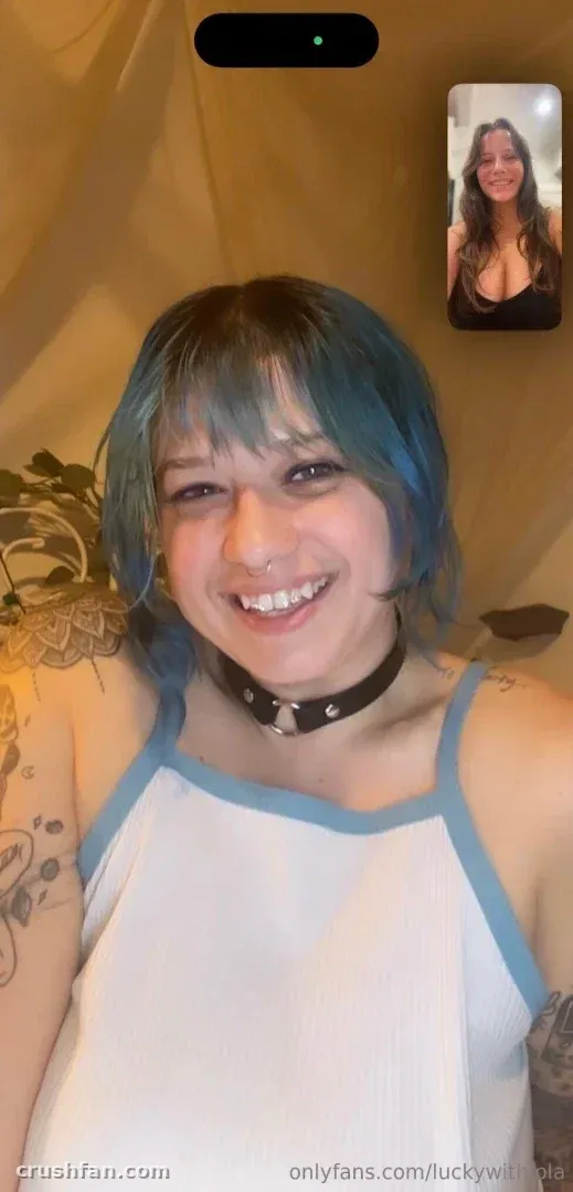 Luckywithlola avec des cheveux bleus et un choker souriant dans un selfie décontracté en intérieur.