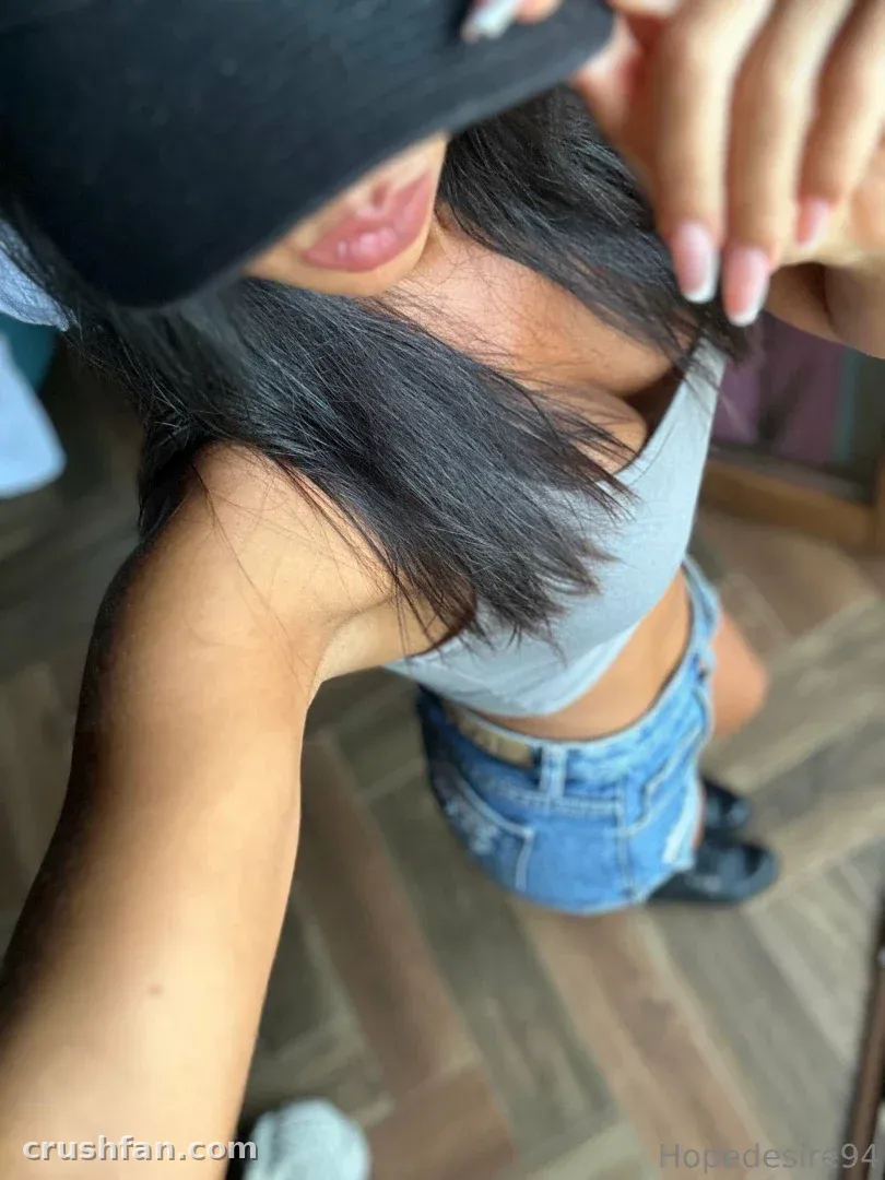 Selfie aus der Vogelperspektive von einer Frau mit schwarzer Cap, grauem Crop-Top und Jeansshorts in Innenräumen