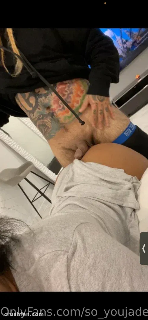 Jade in a black top and dark underwear with a large colourful tattoo, photographed indoors at a low angle.