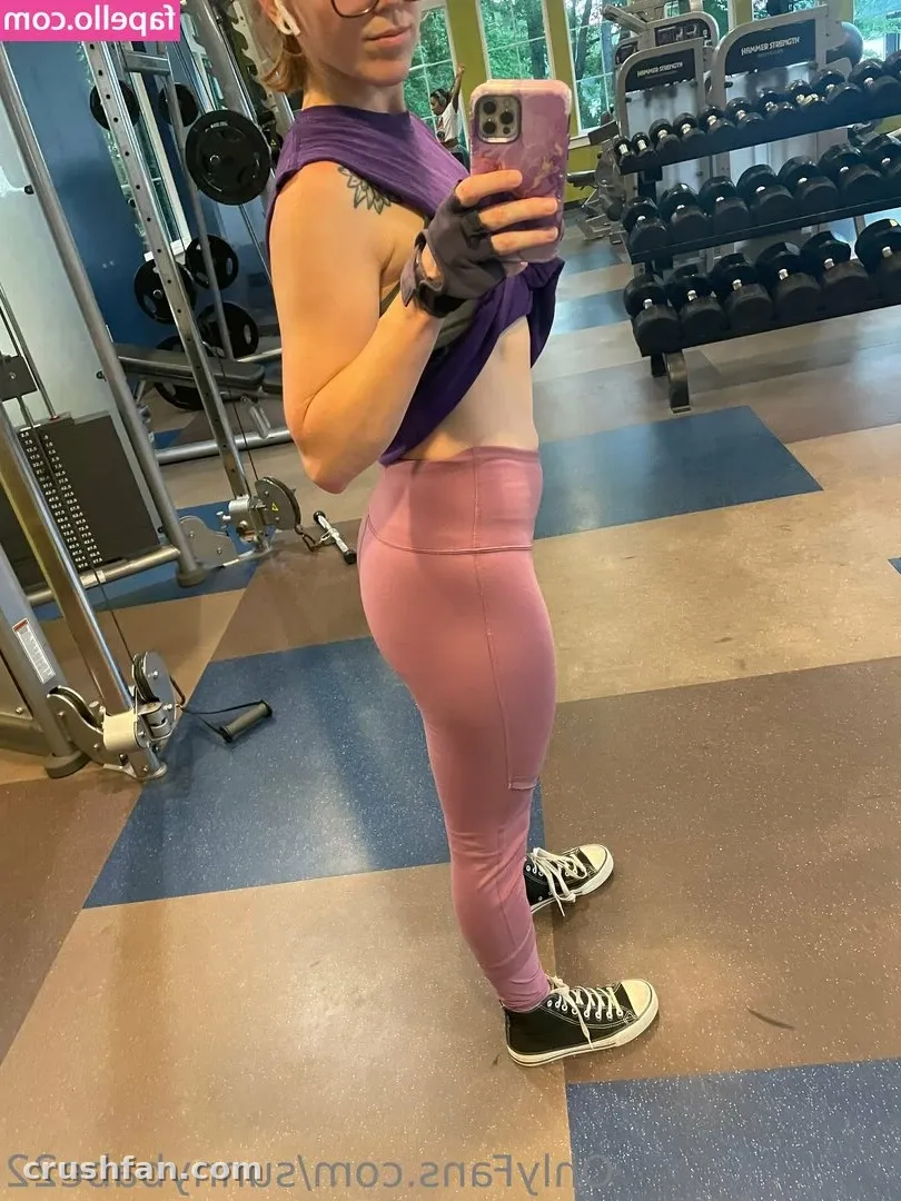Sweet Sunny in a gym mirror selfie wearing a purple top and pink leggings.