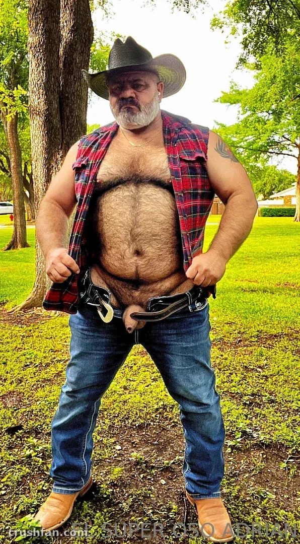 Creator in a cowboy hat and open plaid shirt standing on a grassy lawn with trees behind him