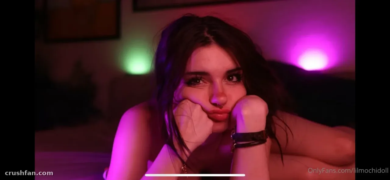 Lil Doll lying down in pink and green neon light, resting her chin on her hand