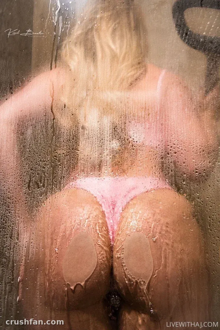 Blonde woman in pink lingerie seen through a wet, steamy glass shower panel