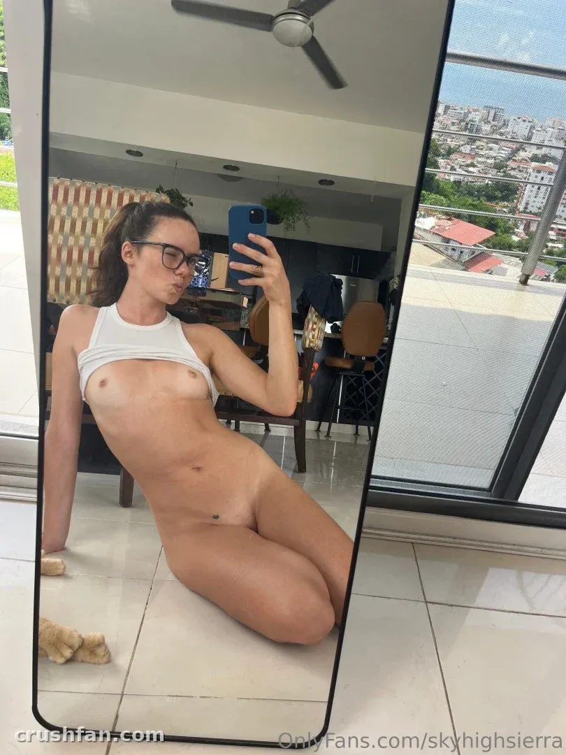 Sierra taking a mirror selfie while reclining on a tiled floor in a bright apartment.
