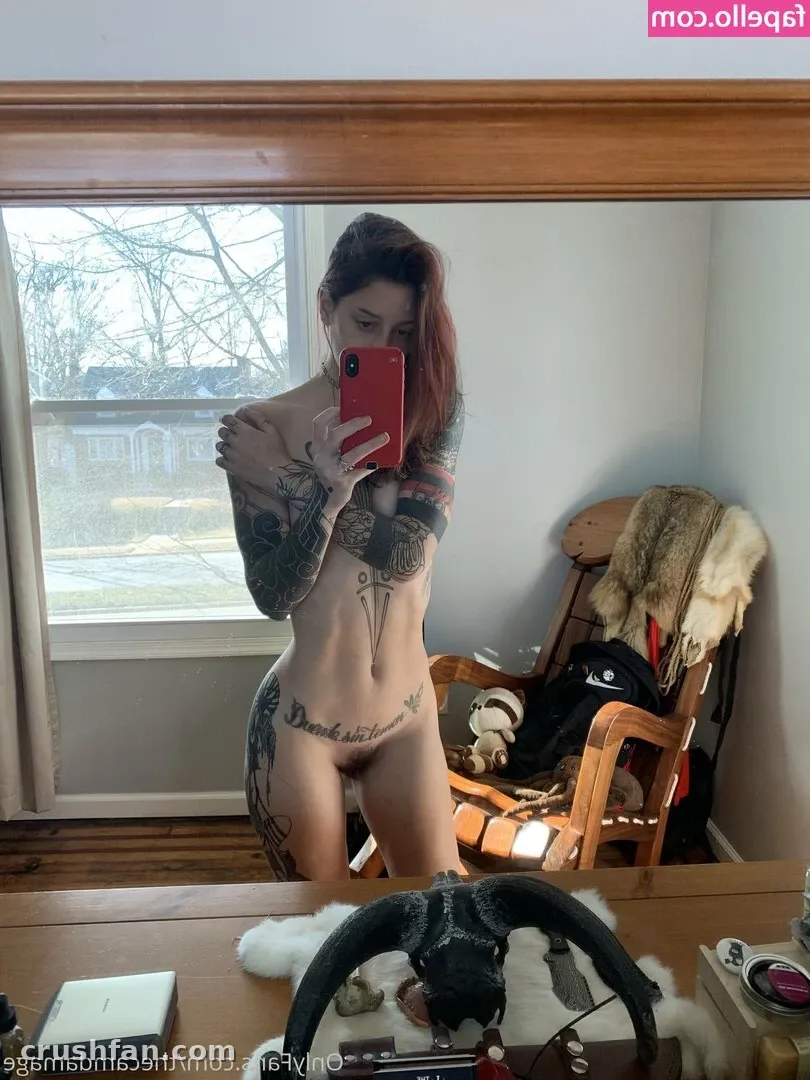 Cam Damage takes a mirror selfie in a room with a window and wooden chair.