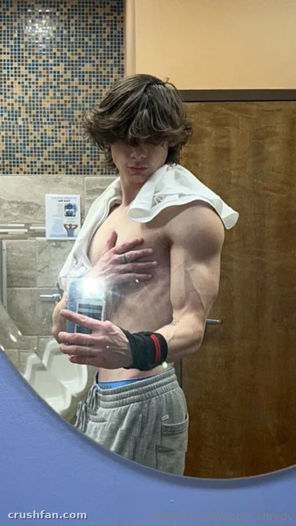 NATHAN tirando uma selfie no espelho em um banheiro com azulejos e uma toalha sobre os ombros