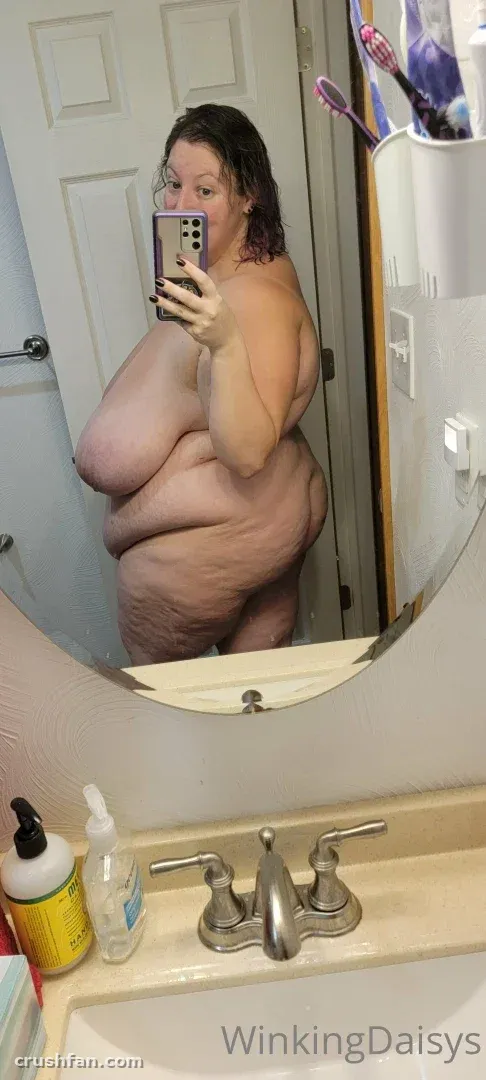 MsTriggaHappy se toma una selfie frente al espejo en un baño, sosteniendo un teléfono.