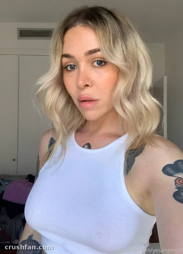 Mujer rubia con una camiseta sin mangas blanca y tatuajes en los brazos en interiores