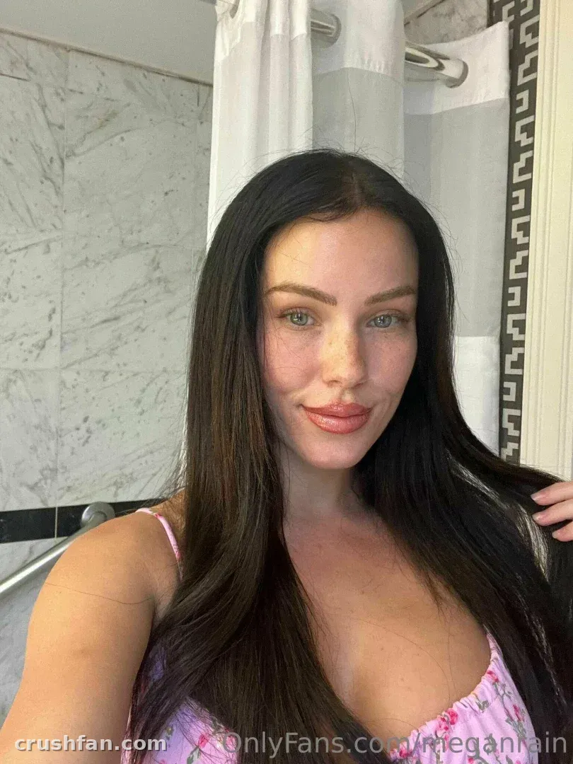 Megan Rain taking a close selfie in a bathroom, wearing a pink floral top.