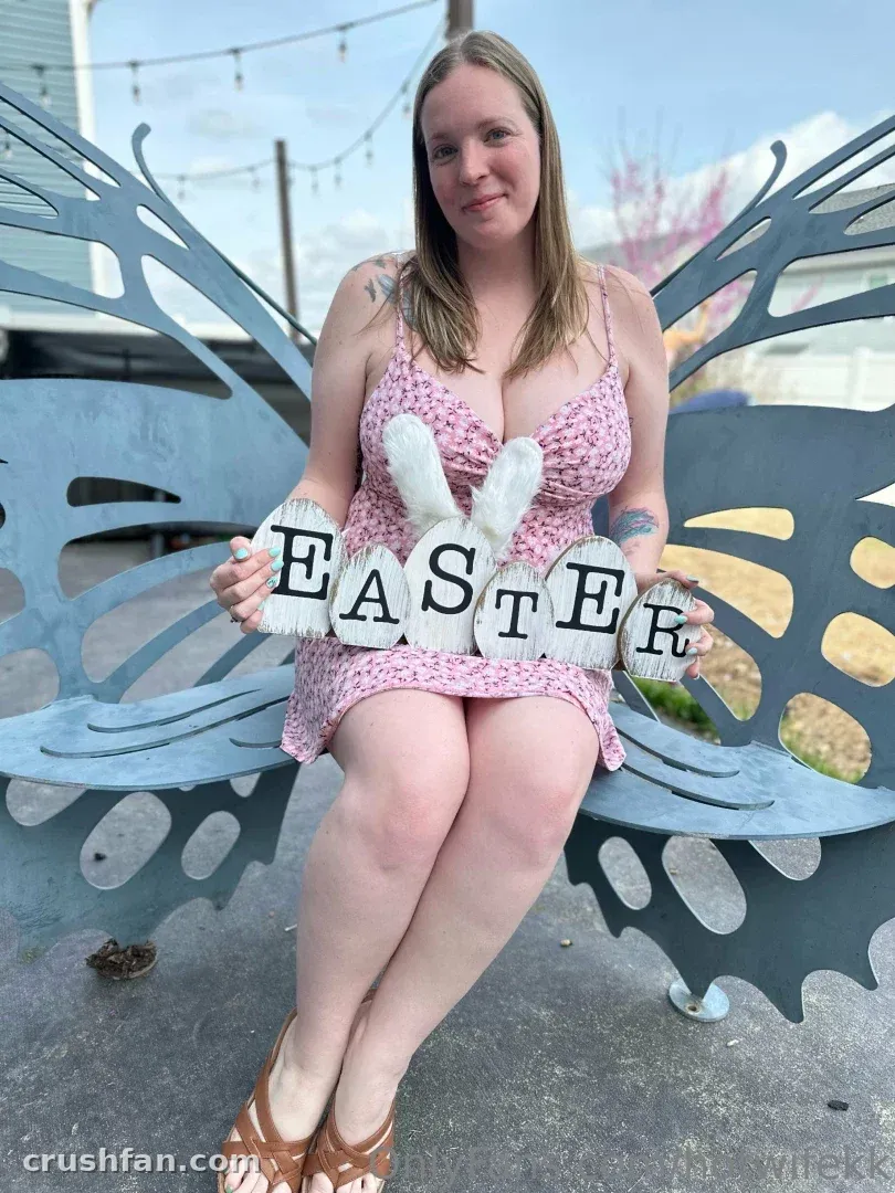 Hotwifekk in a pink floral dress holding Easter letters on a blue butterfly bench