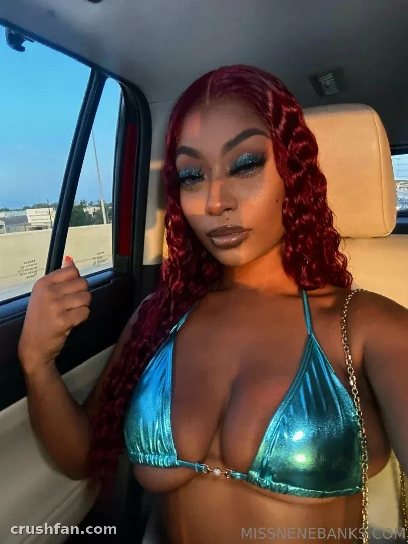Criadora com um top de biquíni turquesa brilhante sentada em um carro, com cabelo ruivo ondulado e maquiagem marcante.
