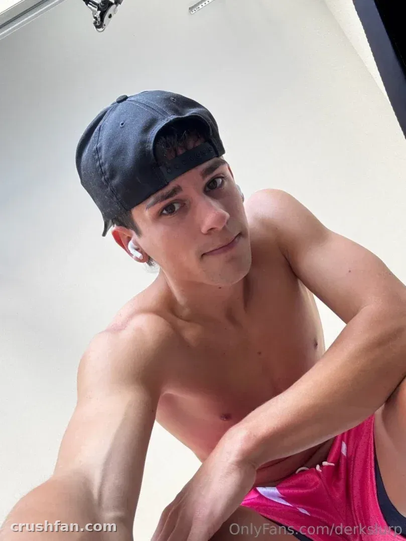 Shirtless creator in a black cap and pink shorts taking a close selfie indoors