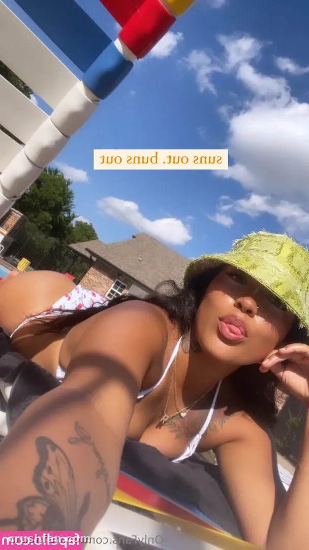Créatrice en bob vert citron et haut blanc prenant un selfie ensoleillé en extérieur sous un ciel bleu.