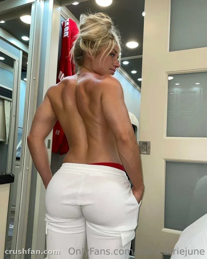 Misscarriejune con pantalones deportivos blancos de pie en un vestuario luminoso con una prenda roja detrás de ella.