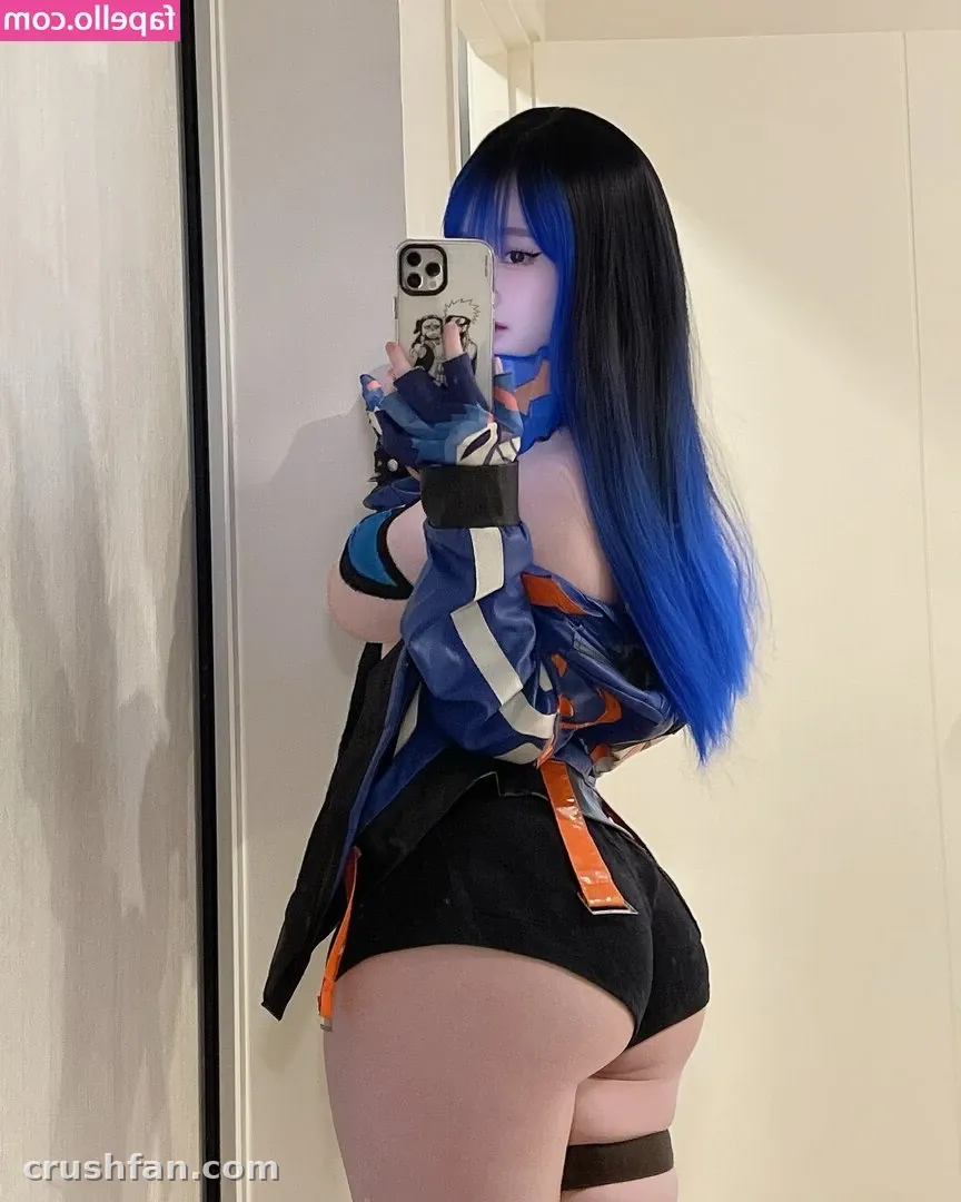 Criadora com um cosplay azul e preto tirando uma selfie no espelho diante de uma porta branca