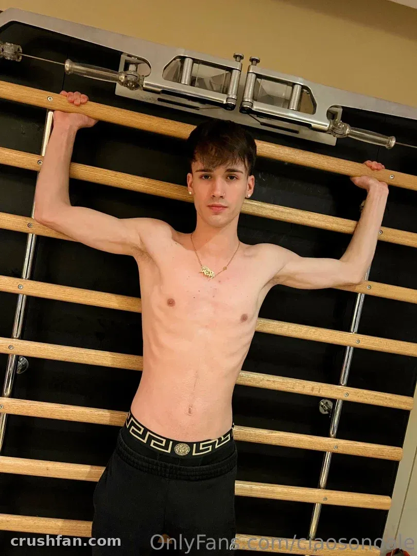 Alex shirtless at wooden wall bars in a gym, wearing black underwear and a necklace