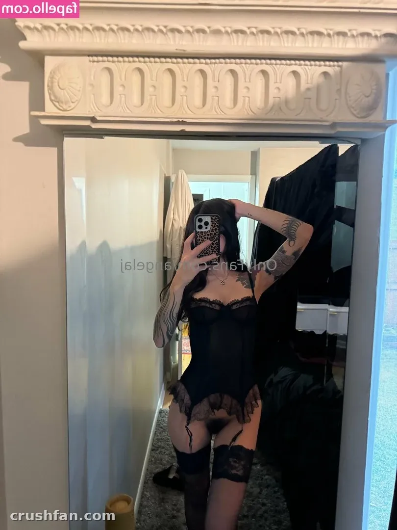 AJ in a black lace bodysuit and stockings taking a mirror selfie in a bright room