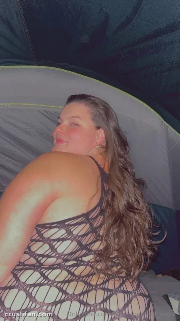 Miss Bunny in a black fishnet top inside a tent, turned in profile with long wavy hair.