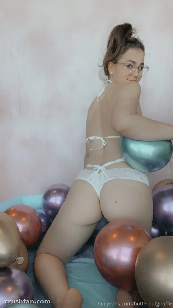 Kayla en lingerie blanche posant parmi des ballons métalliques brillants contre un mur pastel