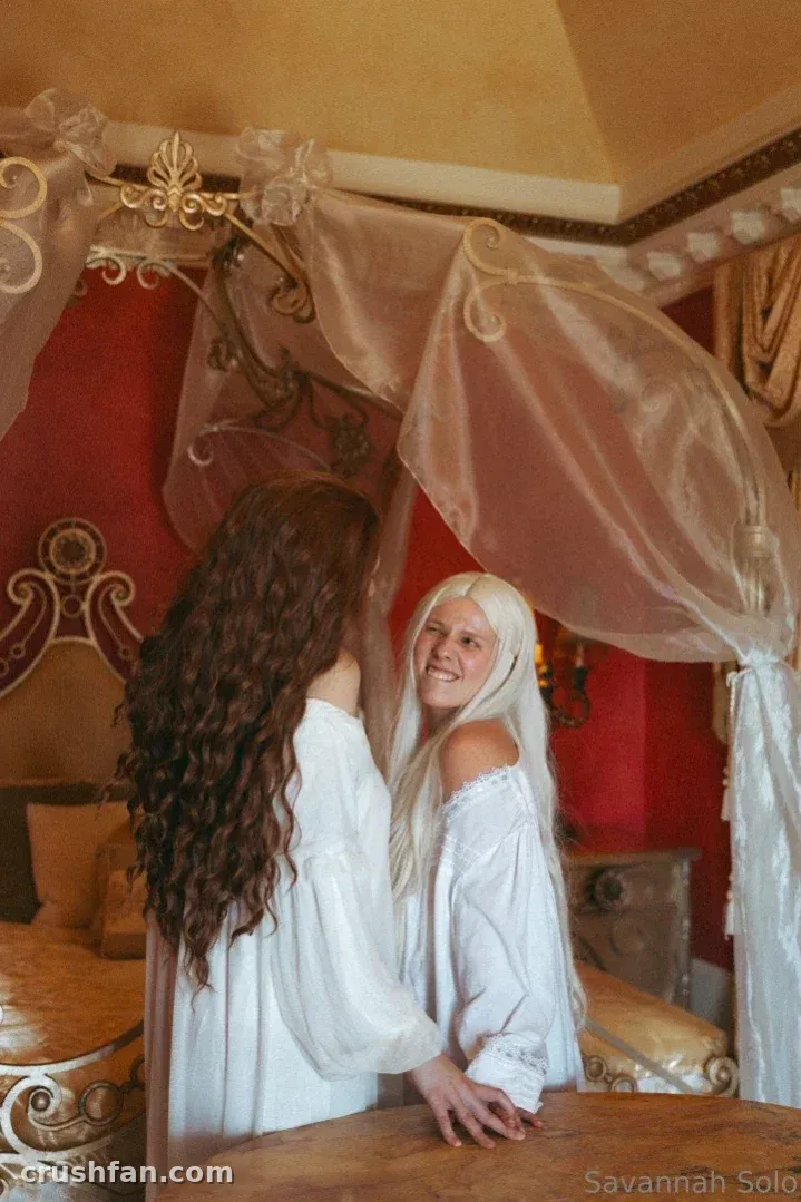 Savannah Solo em um vestido branco ao lado de uma cama com dossel em um quarto vermelho