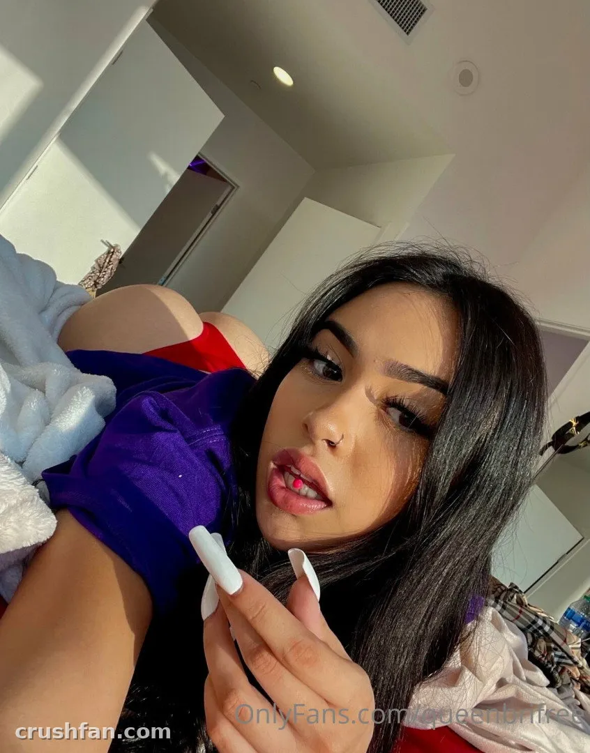 Queen Bri in a purple top taking a close selfie in a bright white room