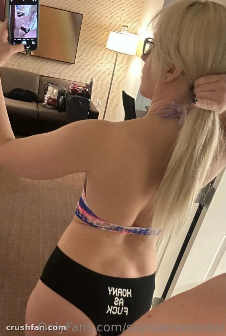 Sophia Rose em um quarto de hotel tirando uma selfie no espelho com um top de biquíni tie-dye e parte de baixo preta