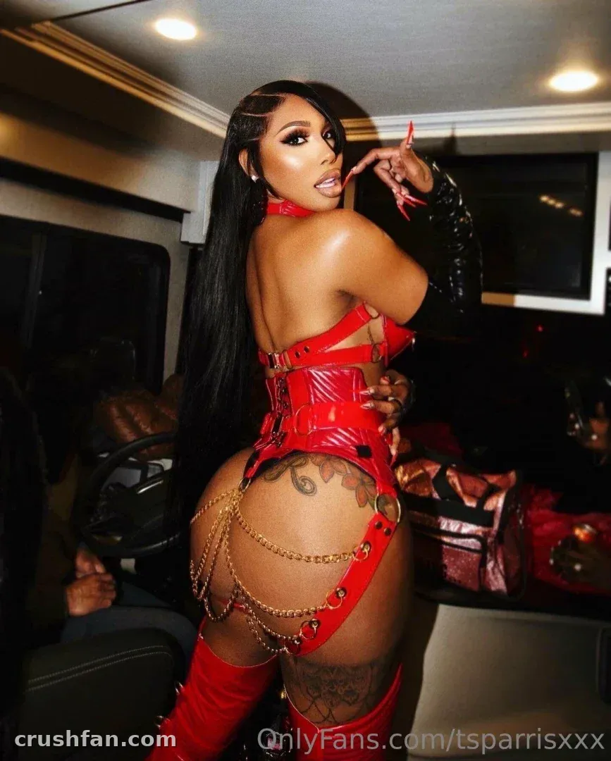 Creator in a shiny red latex outfit with gold chains posing inside a vehicle