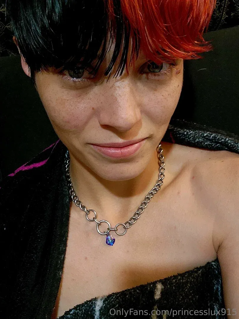 Princess Lux em um retrato em close-up com cabelo vermelho e preto e um colar de prata