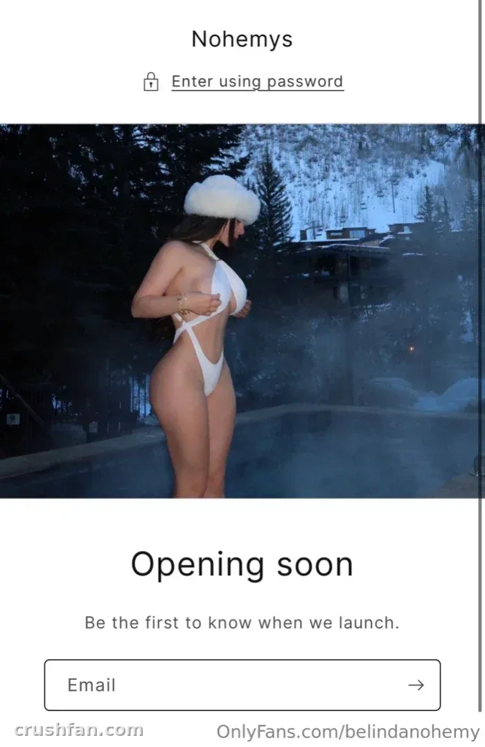 Belinda in einem weißen Badeanzug und flauschigem Hut an einem nebligen Pool zwischen dunklen Bäumen.