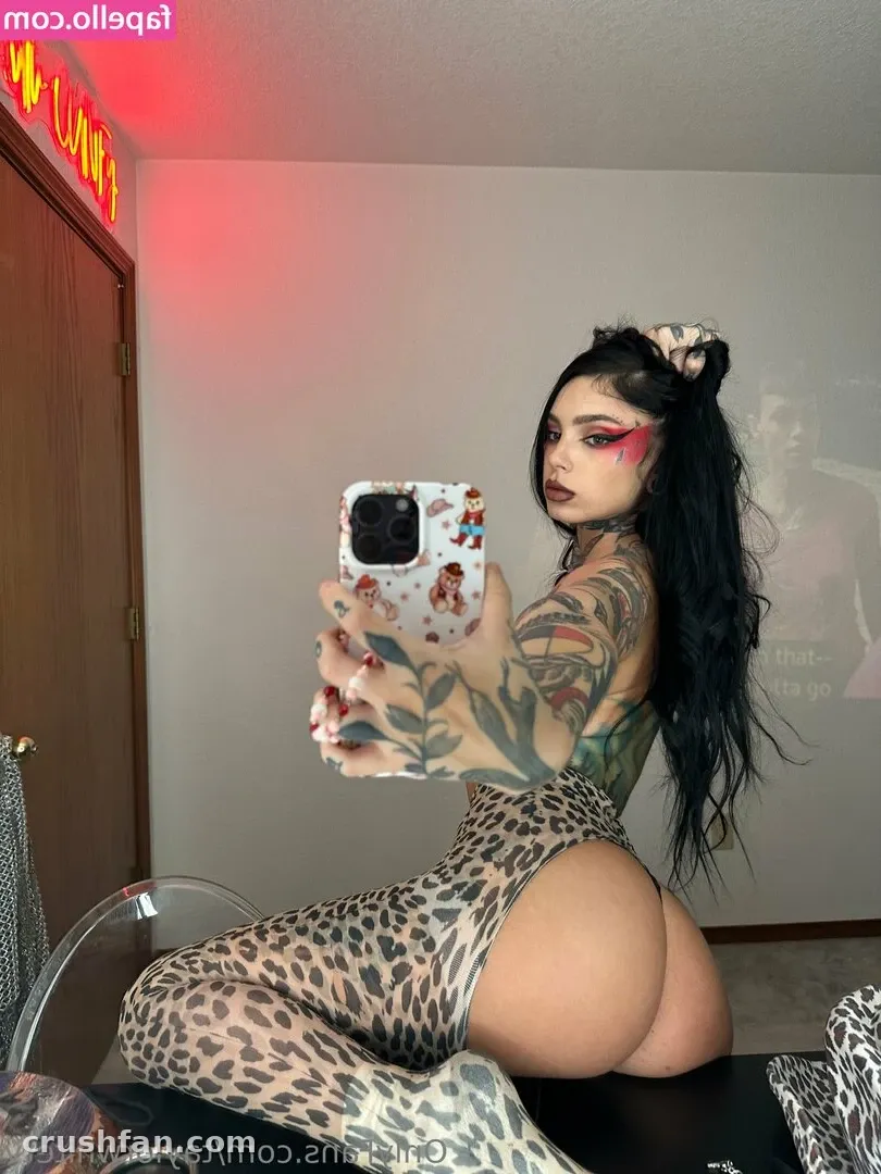 Taylor White en bodysuit imprimé léopard prenant un selfie dans le miroir dans une pièce éclairée en rose.