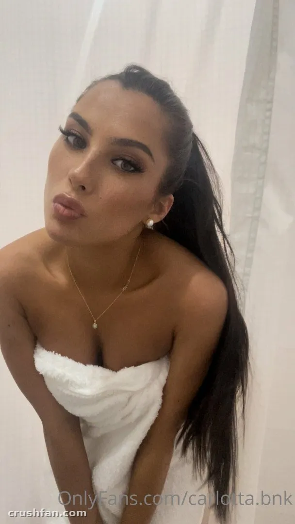 Carlotta in a white towel with a gold necklace against a light background
