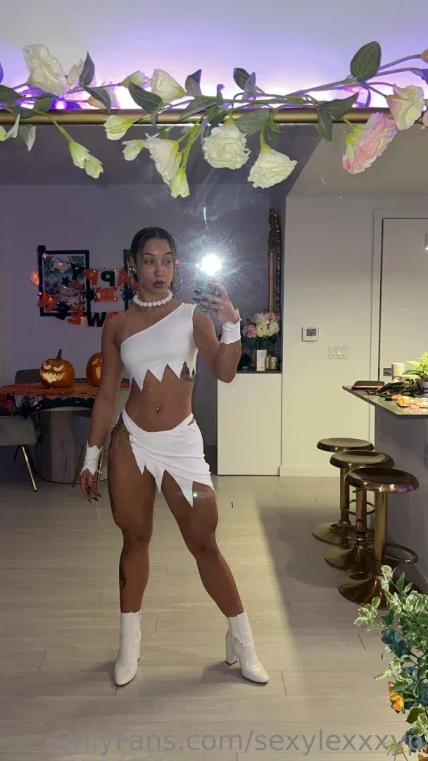 Lexi #1 Puerto Rican en OF con un disfraz blanco tomándose una selfie en el espejo en una habitación decorada.