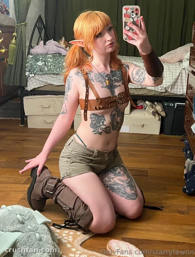 starryfawnn in fantasy cosplay with a leather harness and boots kneeling on a wooden floor