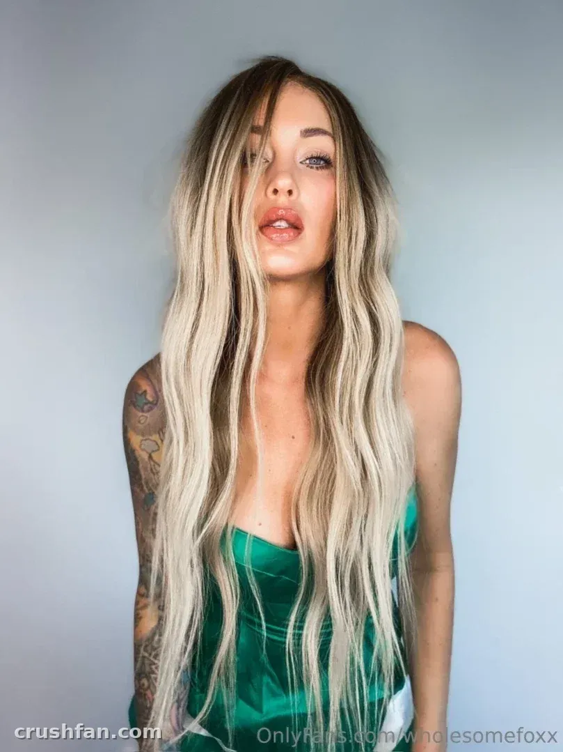 Wholesome Fox in a green top with long blonde hair against a grey studio wall
