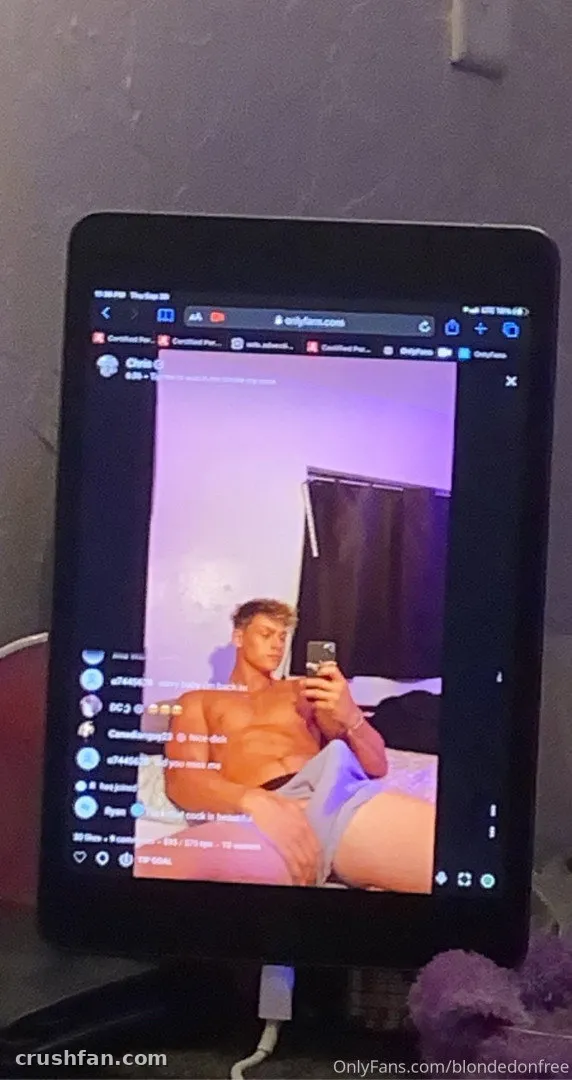 Closer Look Men Free sentado em uma cama, sem camisa e de shorts cinza, mostrado na tela de um tablet.