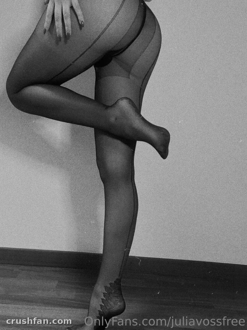 Foto en blanco y negro de Julia Voss de pie sobre un suelo de madera con medias oscuras y transparentes.