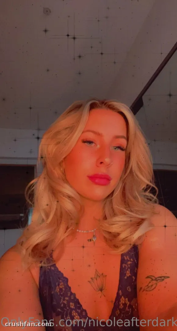 Nicole Garringer taking a warm-toned indoor selfie in a purple lace top.
