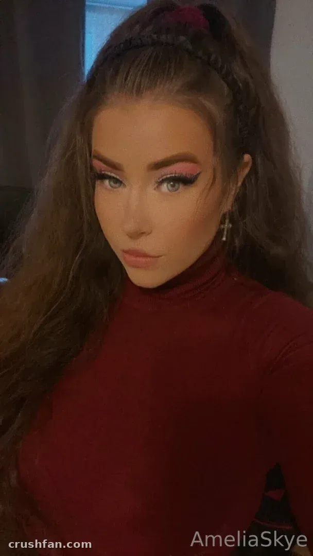 Amelia Skye em uma gola alta vinho com um penteado trançado, olhando para a câmera