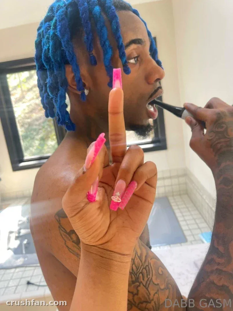 DABB LAND mit blauen Dreadlocks beim Zähneputzen, lange rosa Nägel im Vordergrund in einem Badezimmer.